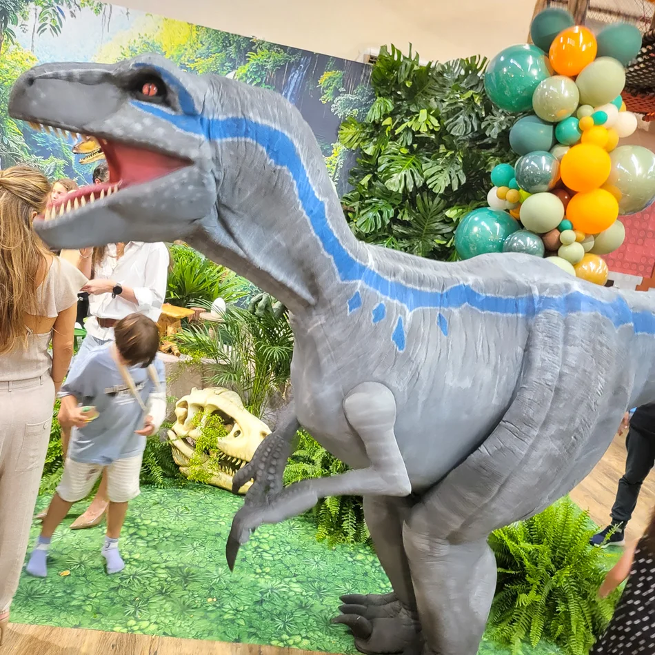 Criança posando para foto com a Velociraptor Blue Personagem Vivo em salão de festas